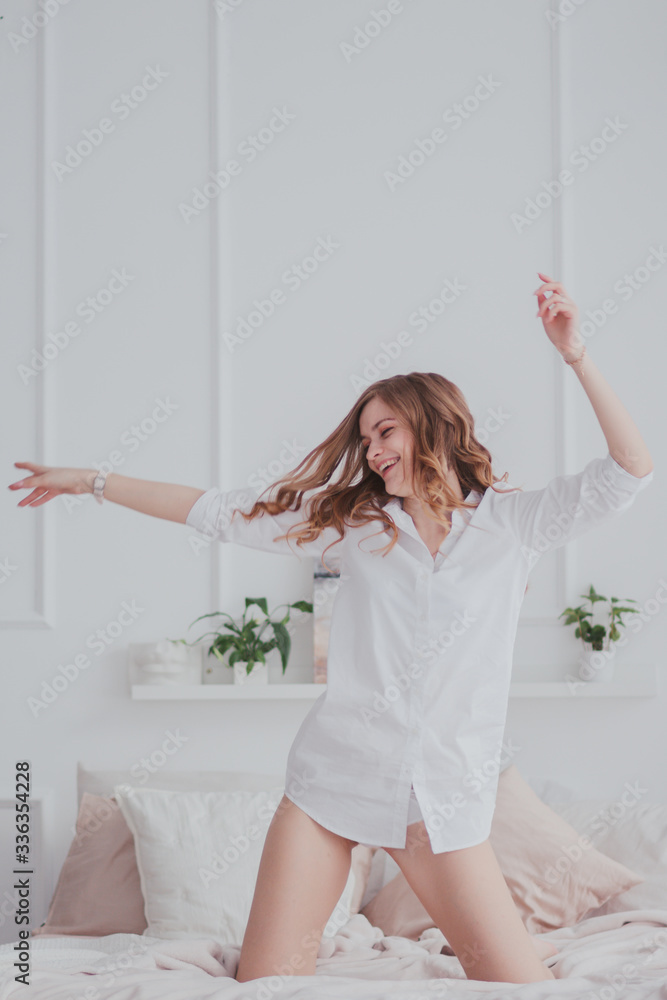 Young pretty woman in white shirt standing in a bed, waving her hands and laughing Young pretty woman in white shirt standing in a bed, waving her hands and laughing