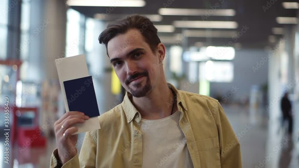 Happy, handsome bearded american man showing passport with flight tickets and waving it. Looking and smilling to the camera while standing at the airport Happy, handsome bearded american man showing passport with flight tickets and waving it. Looking and smilling to the camera while standing at the airport