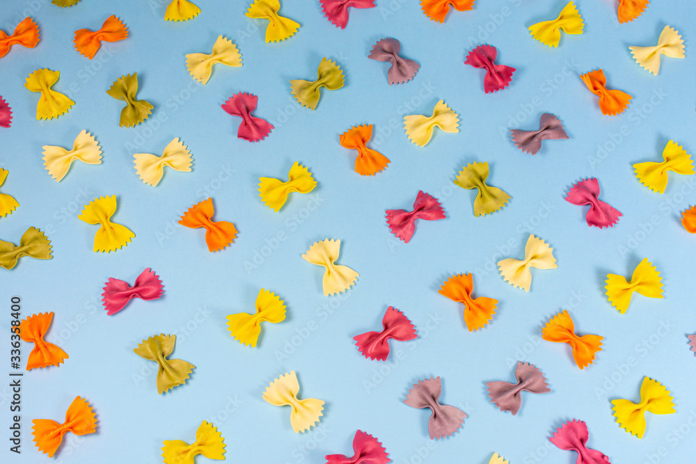 Italian pasta pattern on a blue background. Various colors of bow tie farfalle pasta viewed from above. Top view. Repetition. Italian pasta pattern on a blue background. Various colors of bow tie farfalle pasta viewed from above. Top view. Repetition.