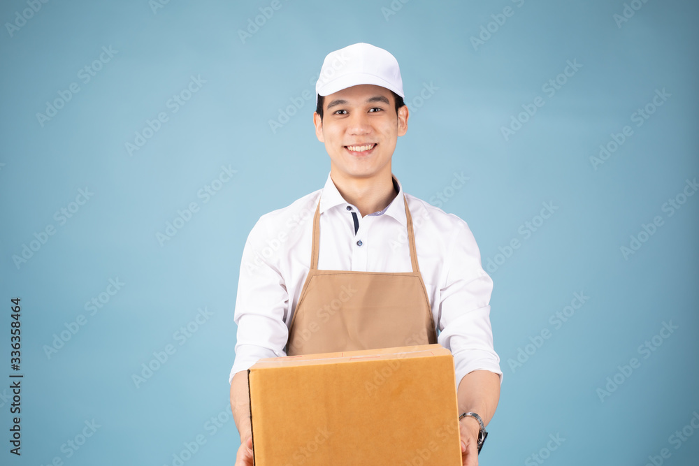 Image of a happy young delivery man in
white cap standing with parcel post box isolated over blue background studio. Image of a happy young delivery man in
white cap standing with parcel post box isolated over blue background studio.
