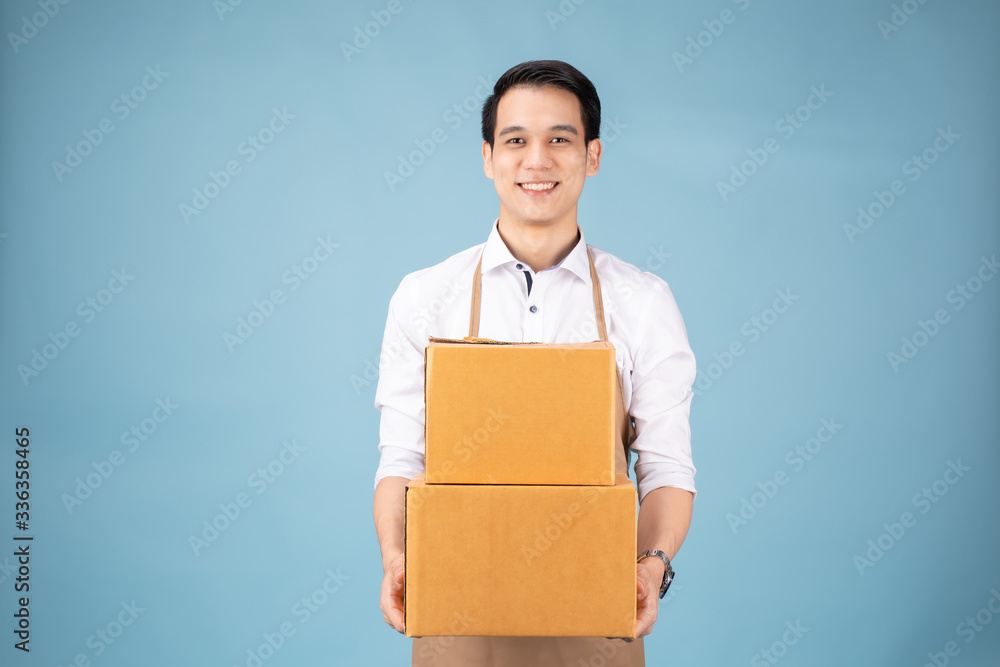 Image of a happy young delivery man in
white cap standing with parcel post box isolated over blue background studio. Image of a happy young delivery man in
white cap standing with parcel post box isolated over blue background studio.