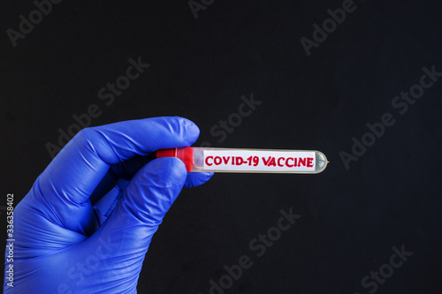 Doctor's hand in a medical glove holds a test tube with the inscription vaccine. Coronavirus drug search concept. Place for text.