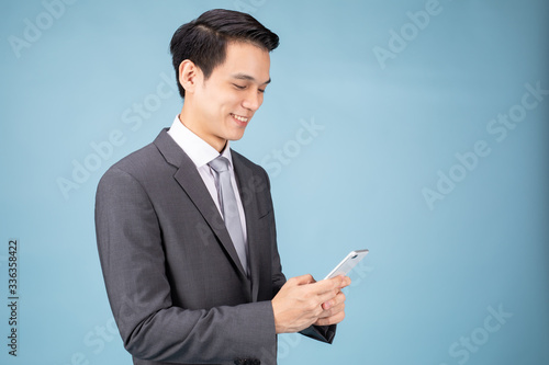Portrait of smiling Asian Businessman holding and using tablet. Blue background studio concept.