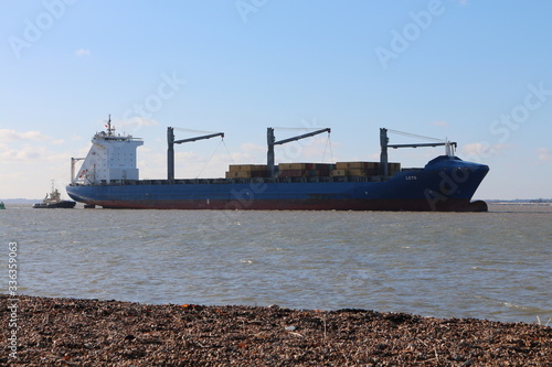 Container ship escorted by tugs approaching Felixstowe Docks in Suffolk, UK.