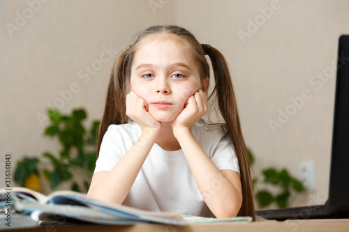 Distance or remote learning. Pupil want to sleep. Tired schoolgirl with hand on face sitting at laptop. Online school.