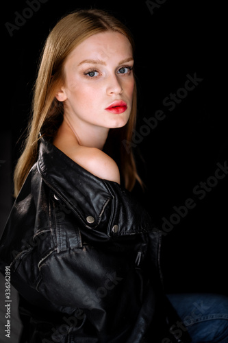 Portrait of a model girl in a black biker leather jacket. young woman with brown hair posing on black background