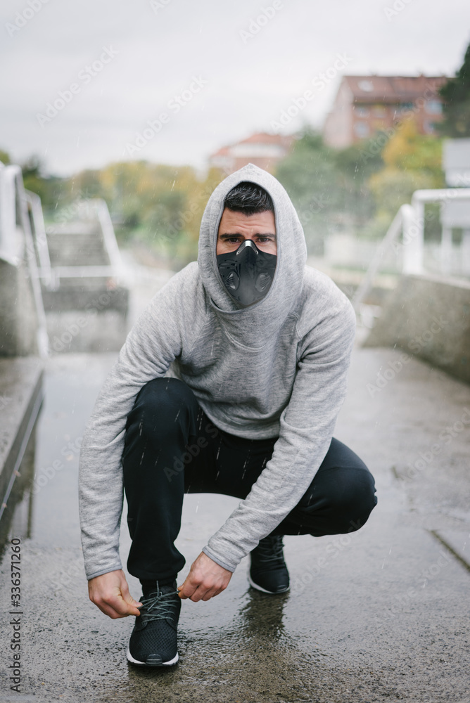 Man ready for urban winter running workout under Sporty man wearing face  mask for protection against coronavirus and pollution during winter running  and outdoor fitness workout under the rain. Sport Stock Photo