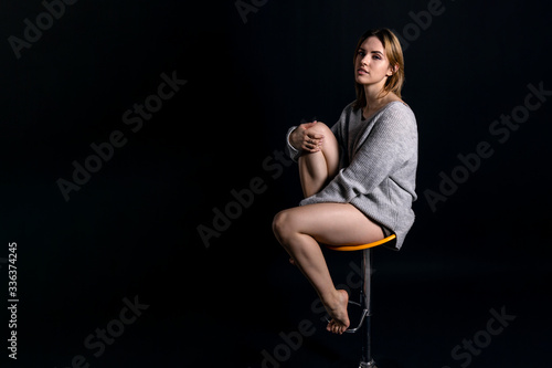 young beautiful girl in a gray sweater with a calm pensive facial expression sits on a dark background, copy space