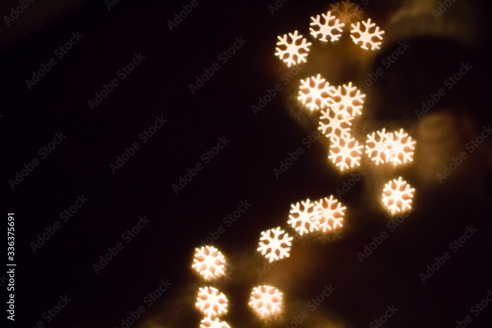 Colorful snowflake bokeh on a dark background, yellow shining snowflake shape bokeh