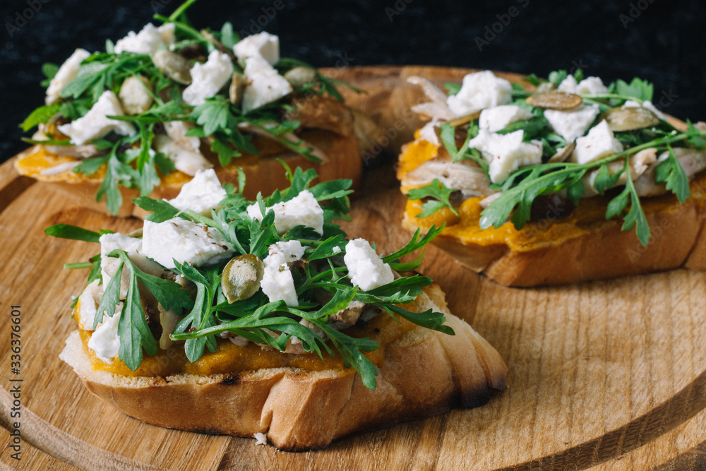 Italian appetizer - bruschetta with with arugula, parsley or cilantro, cheese and chicken on a wooden board