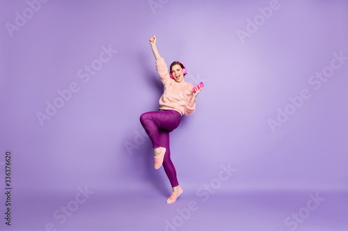 Full size photo of funky lady hold telephone modern earphones on ears listen youth music dance students party wear casual stylish pink pullover trousers isolated purple color background