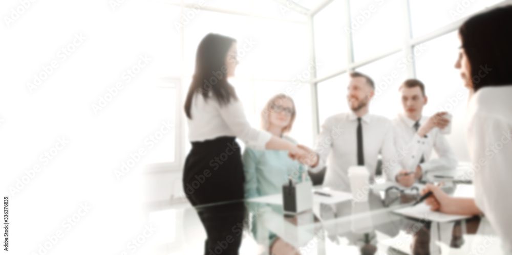 handshake employees near the Desk in the office. Background for text with people in blur handshake employees near the Desk in the office. Background for text with people in blur