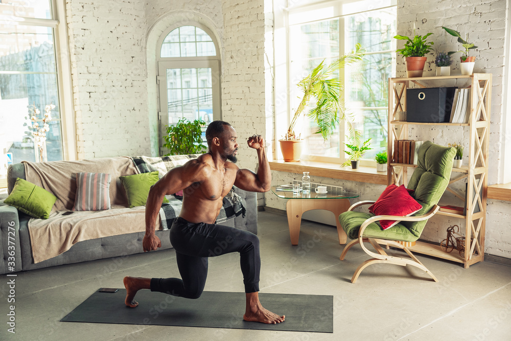 African-american man teaching at home online courses of fitness, aerobic, sporty lifestyle while being quarantine. Getting active while isolated, wellness, movement concept. Training, sit-ups. African-american man teaching at home online courses of fitness, aerobic, sporty lifestyle while being quarantine. Getting active while isolated, wellness, movement concept. Training, sit-ups.