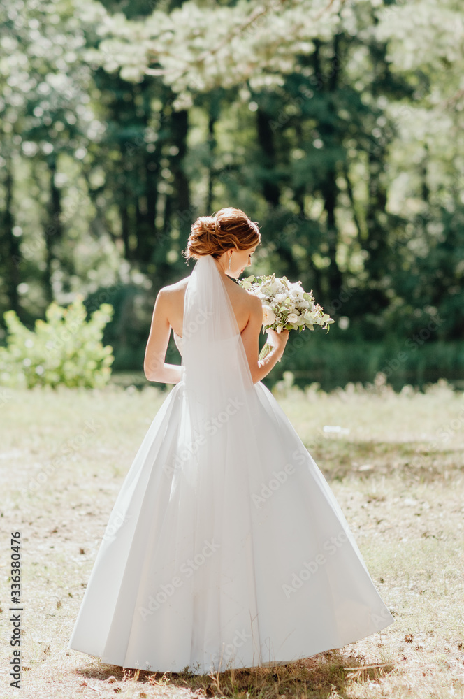 the bride in a white dress stands with her back to us and holds a bouquet of flowers the bride in a white dress stands with her back to us and holds a bouquet of flowers