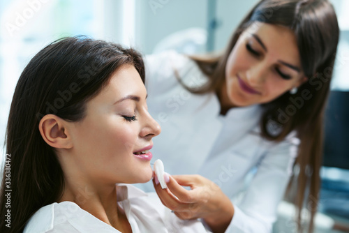 Face injection close up. Syringe with filler for face contouring or augmentation. Cheerful young woman getting botox procedure. Beautician doctor standing near her. Healthcare cosmetology concept