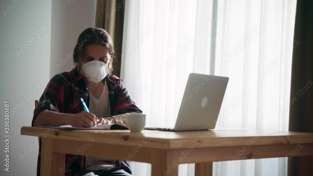 Young woman remote employee in a medical mask working from home using her laptop while in self-isolation. Coronavirus quarantine. Remote working or online self-education concept. Young woman remote employee in a medical mask working from home using her laptop while in self-isolation. Coronavirus quarantine. Remote working or online self-education concept.