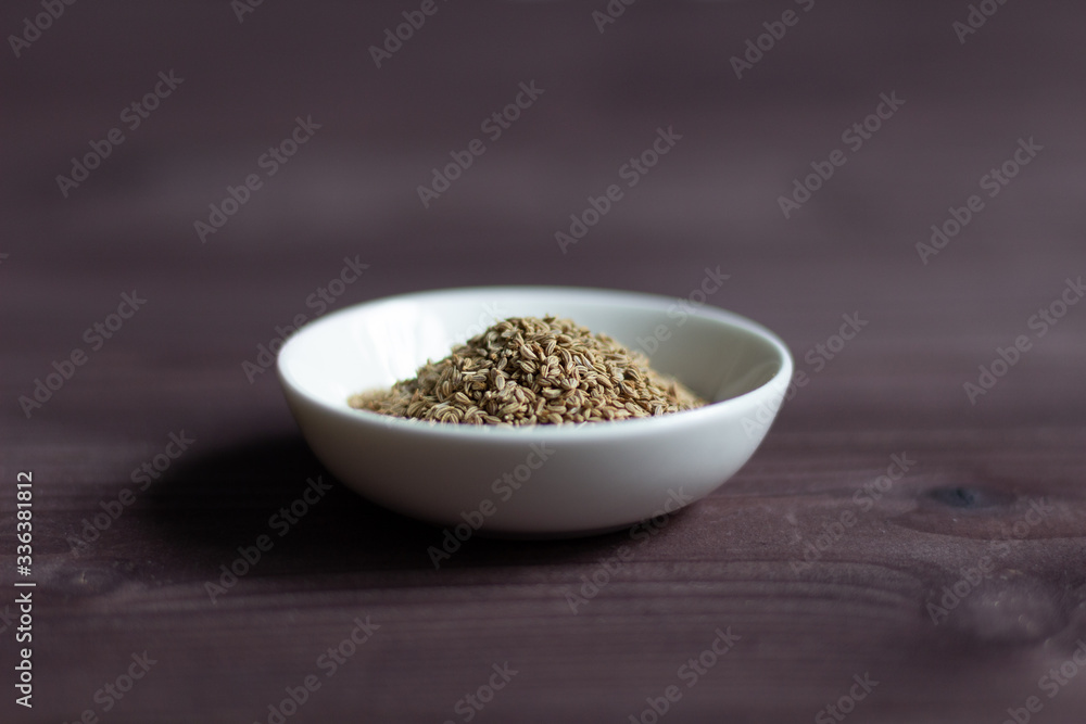 Ajowan seeds in white bowl on brown wooden background Ajowan seeds in white bowl on brown wooden background