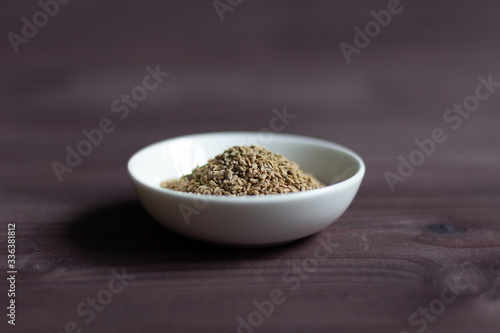 Ajowan seeds in white bowl on brown wooden background
