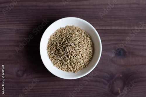 Ajowan seeds in white bowl on brown wooden background, top view
