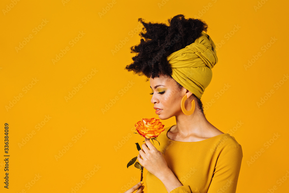 Profile portrait of a beautiful young woman smelling yellow orange rose and looking down, isolated on yellow background - obrazy, fototapety, plakaty 
