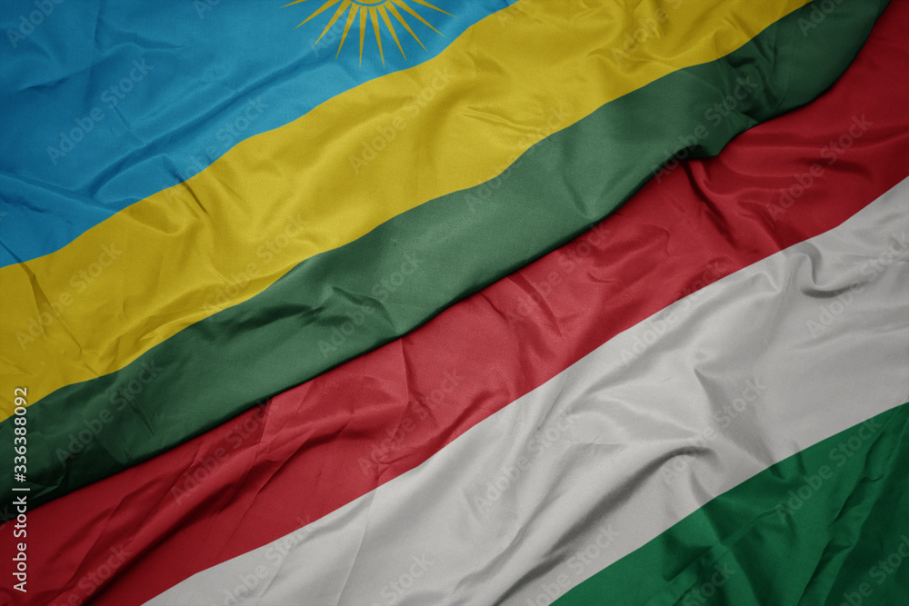 waving colorful flag of hungary and national flag of rwanda.