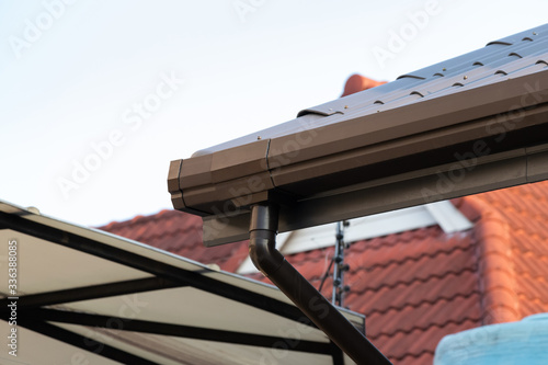 brown metal rain gutter and plastic pipe of house roof.