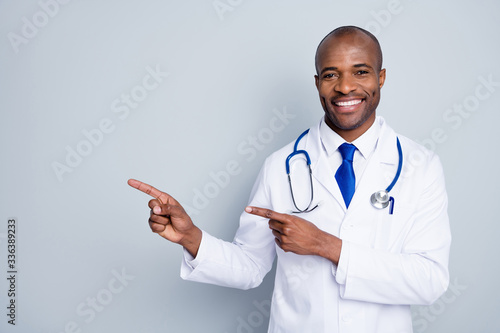 Photo of doctor dark skin guy family doc direct finger empty space advising epidemic rules steps disinfection safety wear lab coat neck tie stethoscope isolated grey color background