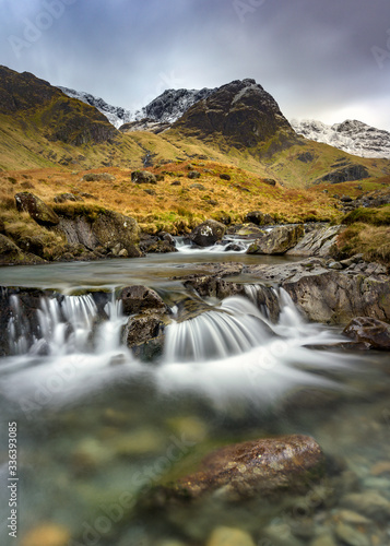 Small Cascading Waterfall Stream At Deepdale Beck In The Lake District National Park With Snow On Mountain Peaks. 