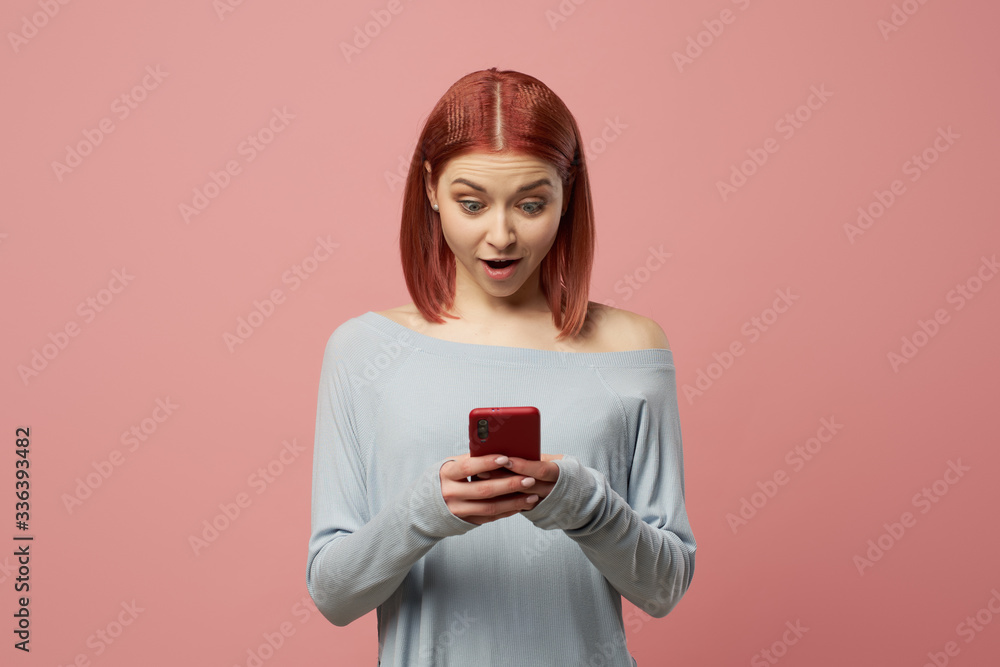 Serious ginger woman with phone in her hands standing in studio Serious ginger woman with phone in her hands standing in studio