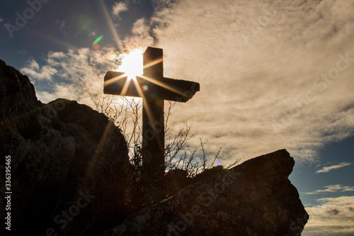 Stone christian cross over a mountain and next to the sun