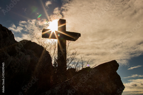 Stone christian cross over a mountain and next to the sun photo