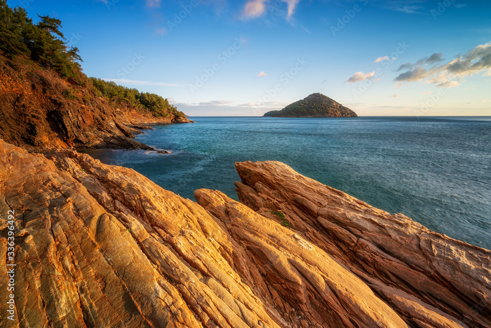 Magnificent sunset view at the rocky coastline of Thasos island and view to little island Nisida Kinira, Greece