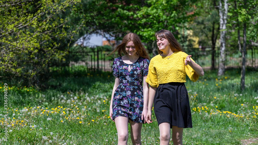 Young girls have fun time in the park. The sisters communicate and share secrets. Happy sisters are enjoying a warm spring day Young girls have fun time in the park. The sisters communicate and share secrets. Happy sisters are enjoying a warm spring day