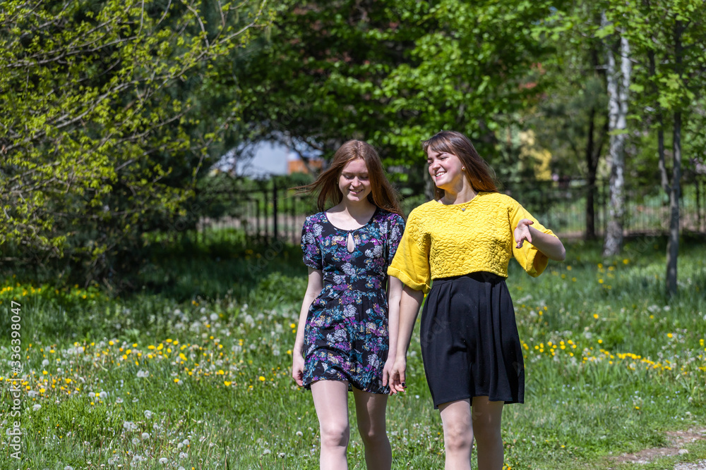 Fototapeta premium Young girls have fun time in the park. The sisters communicate and share secrets. Happy sisters are enjoying a warm spring day