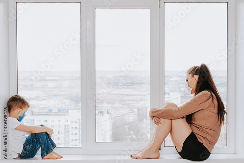 A woman with a child in medical masks is sitting on the window at home in quarantine and looking out the window. Prevention of Coronovirus and Covid -19 Free Download A woman with a child in medical masks is sitting on the window at home in quarantine and looking out the window. Prevention of Coronovirus and Covid -19 - GFXLoad