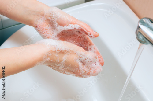 Soapy hands of a young woman who washes hands in the bathroom
