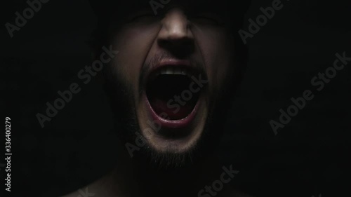 Dark close-up portrait of male mouth screaming on black background.