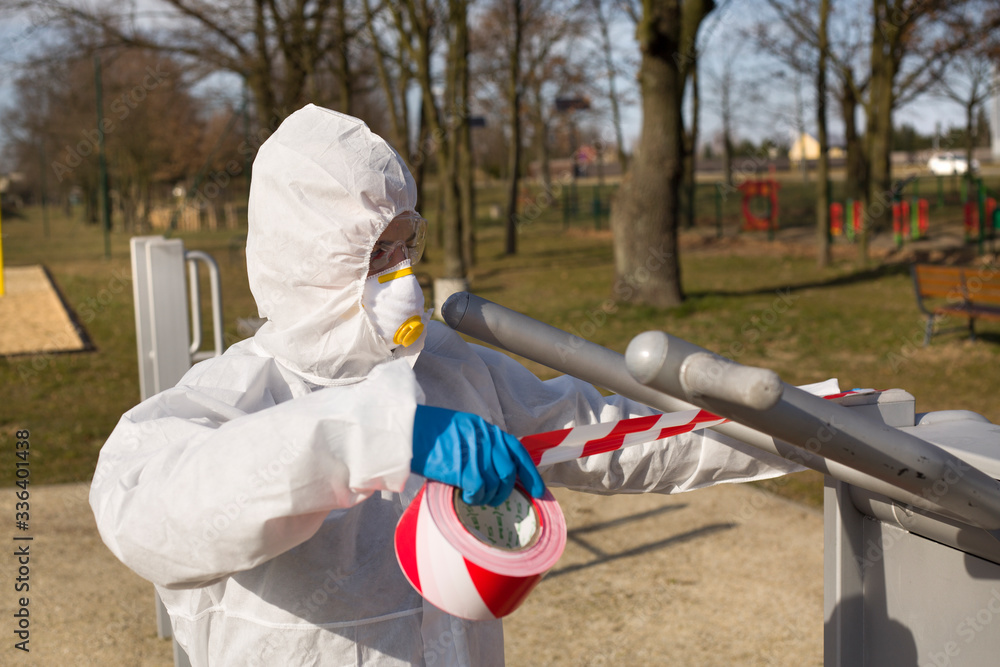 Naklejka premium Kobieta w maseczce i kombinezonie ochronnym zabezpiecza sprzęt sportowy w parku by z niego nie korzystać
