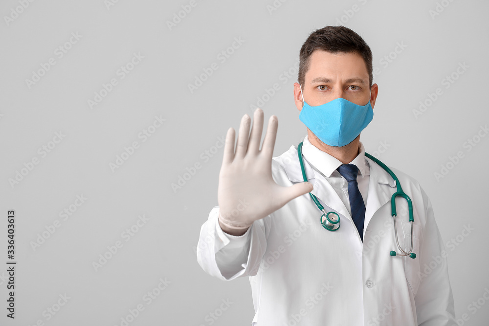Doctor in protective medical mask showing STOP gesture on grey background Doctor in protective medical mask showing STOP gesture on grey background