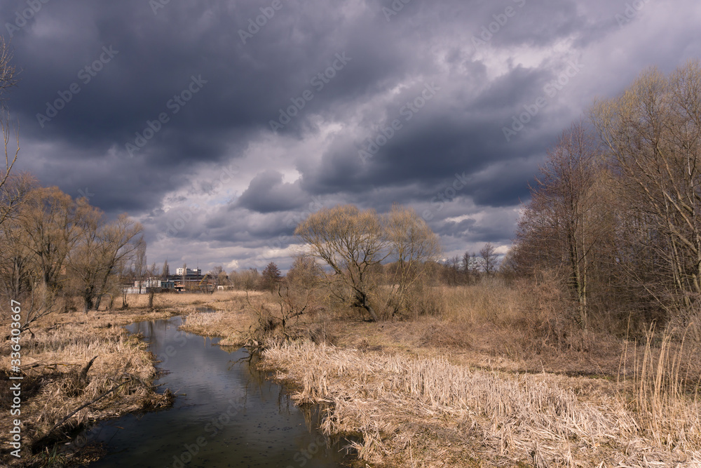 Dramatic autumn landscape with cloudy sky reflecting in river, dry and naked grass and trees on riverside, and distant abandoned buildings. Concept of crisis. Dramatic autumn landscape with cloudy sky reflecting in river, dry and naked grass and trees on riverside, and distant abandoned buildings. Concept of crisis.
