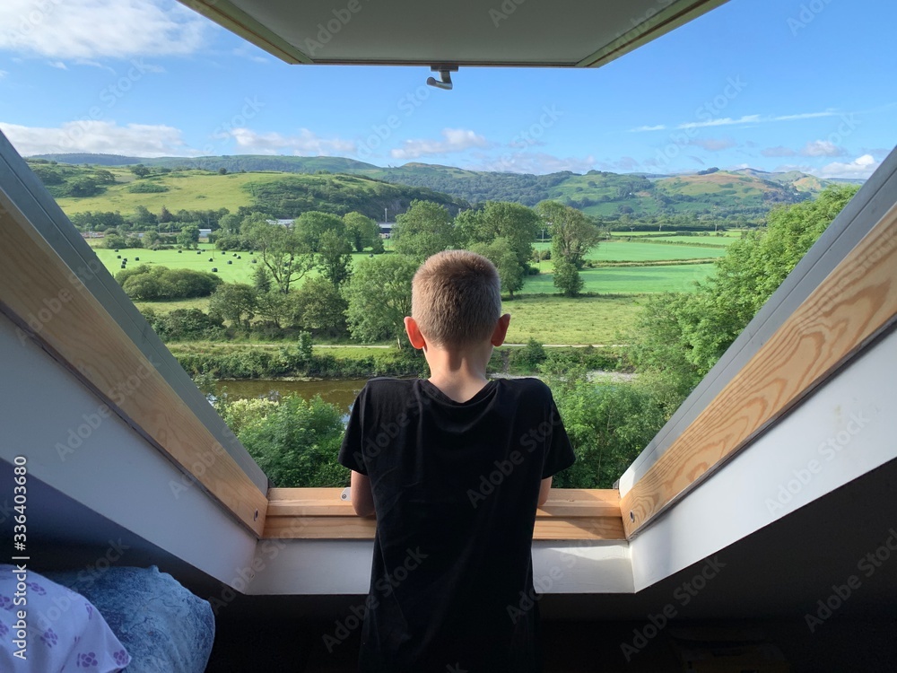 Φωτογραφία Boy looks out of a Velux window over a beautiful green valley on a summers morni