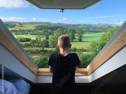 Boy looks out of a Velux window over a beautiful green valley on a summers morning
