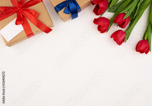 bouquet of red blooming tulips with green leaves, wrapped gift in brown craft paper on a white background