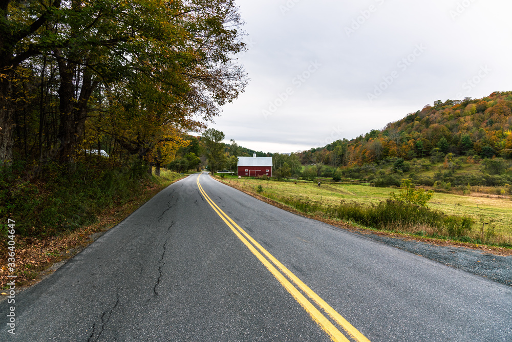 Empty straight road in the countryside on a cloudy autumn day. A red barn is visible on the right side of the road. Empty straight road in the countryside on a cloudy autumn day. A red barn is visible on the right side of the road.