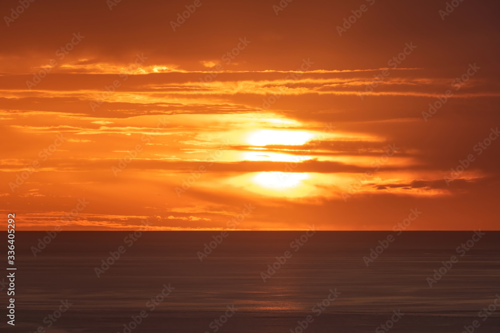 Long aerial view of distorted sunset sun disk behind layered clouds over ocean horizon