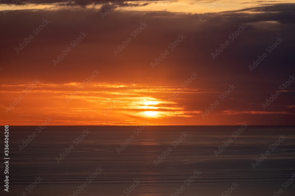 Aerial view of distorted sunset sun disk behind layered clouds over ocean horizon