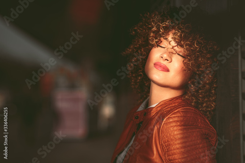 Portrait of a young woman in a brown leather jacket with blond afro curly hair on the street