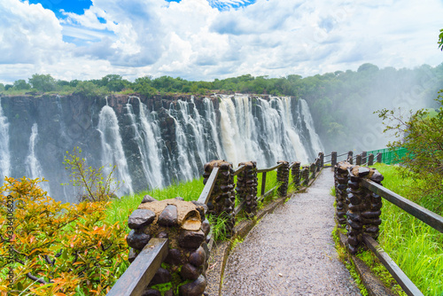 Walking way with view to the dramatic clouds and waterfall at Victoria Falls on the Zambezi River, Zimbabwe, Zambia. photo