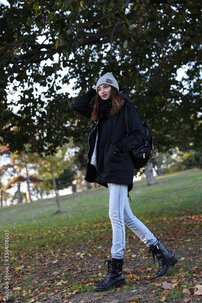 Model in a black coat and grey hat with a backpack. A woman in the fall in a new York city Park