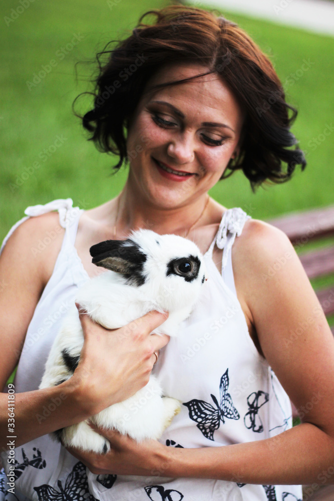 woman in a white blouse with butterflies and a colorful skirt sits on a bench with a white rabbit in her arms woman in a white blouse with butterflies and a colorful skirt sits on a bench with a white rabbit in her arms